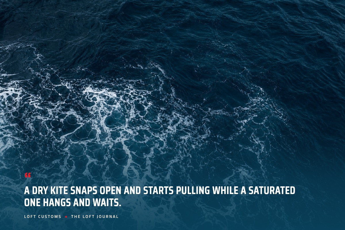 Pull quote over aerial ocean water: A dry kite snaps open and starts pulling while a saturated one hangs and waits. Loft Customs, The Loft Journal